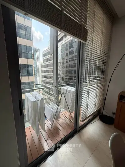 Modern apartment balcony with city view and laundry drying, featuring floor-to-ceiling windows and sleek blinds.