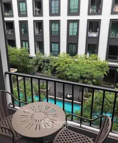 Charming balcony view overlooking lush greenery and a serene pool in a modern apartment complex.