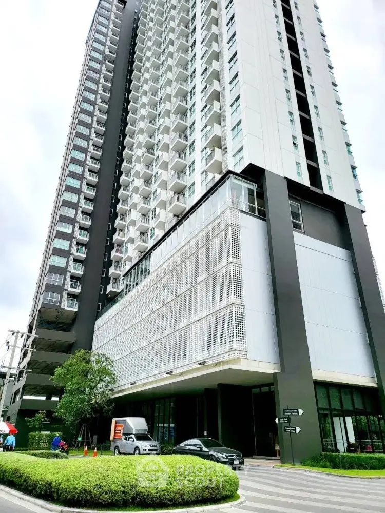 Modern high-rise building with sleek design and lush greenery at entrance