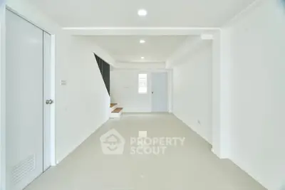 Spacious minimalist living room with sleek white tiles and modern staircase.