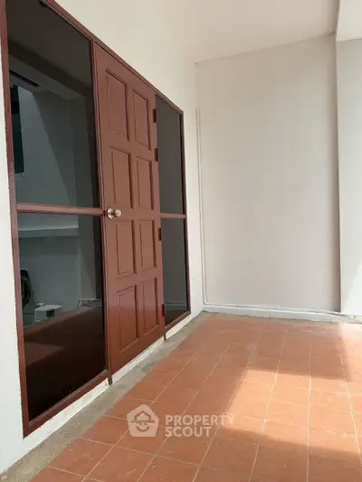 Spacious balcony with terracotta tiles and wooden door, perfect for relaxation.