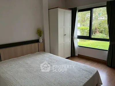 Cozy bedroom with large window overlooking lush garden, featuring a white wardrobe and elegant decor.