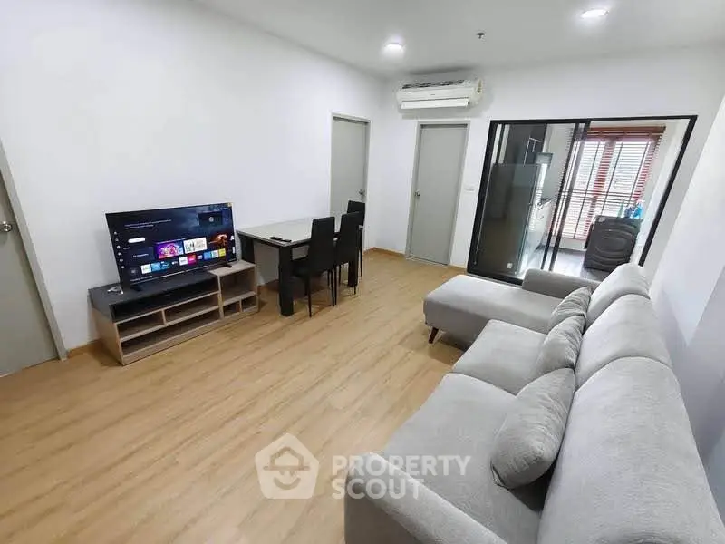 Modern living room with cozy gray sofa, flat-screen TV, and dining area in open layout apartment.
