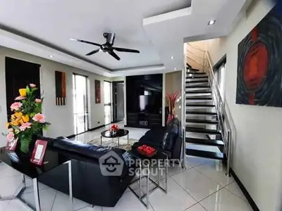 Modern living room with sleek black furniture and stylish decor, featuring a staircase and ceiling fan.