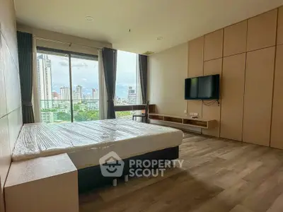 Spacious modern bedroom with city view and wall-mounted TV in high-rise apartment.