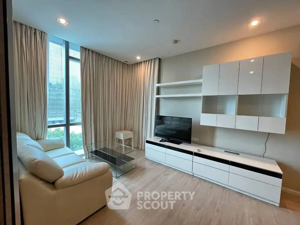 Modern living room with sleek white furniture and large windows offering natural light.