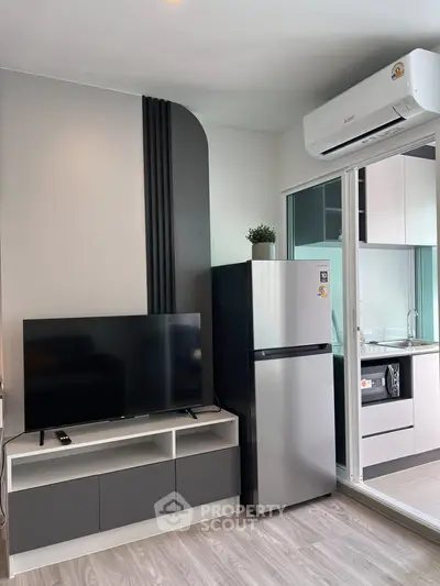 Modern living room with sleek TV unit and stainless steel fridge, adjacent to a stylish kitchen.