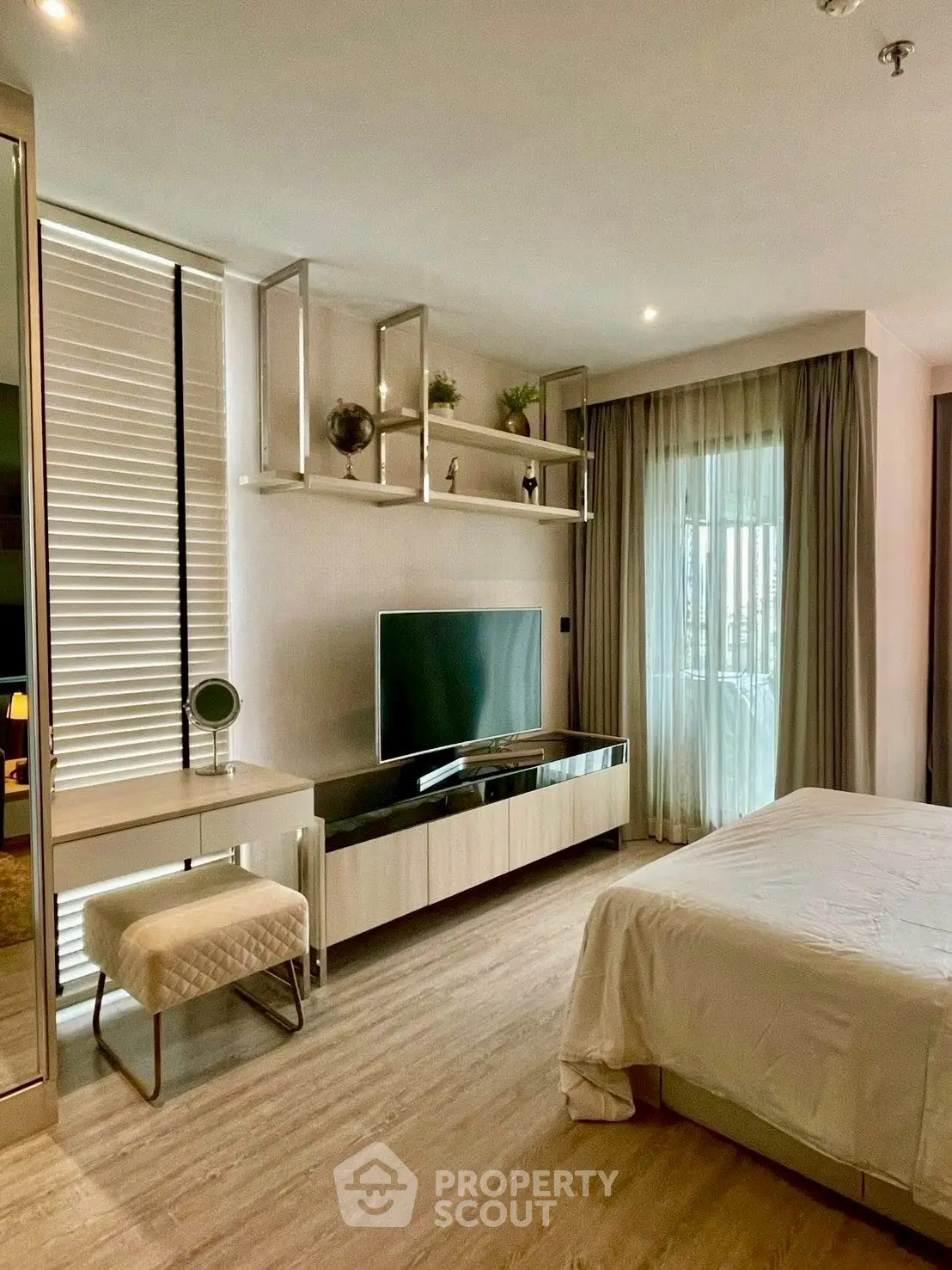 Modern bedroom with sleek decor and large TV, featuring natural light and stylish furnishings.