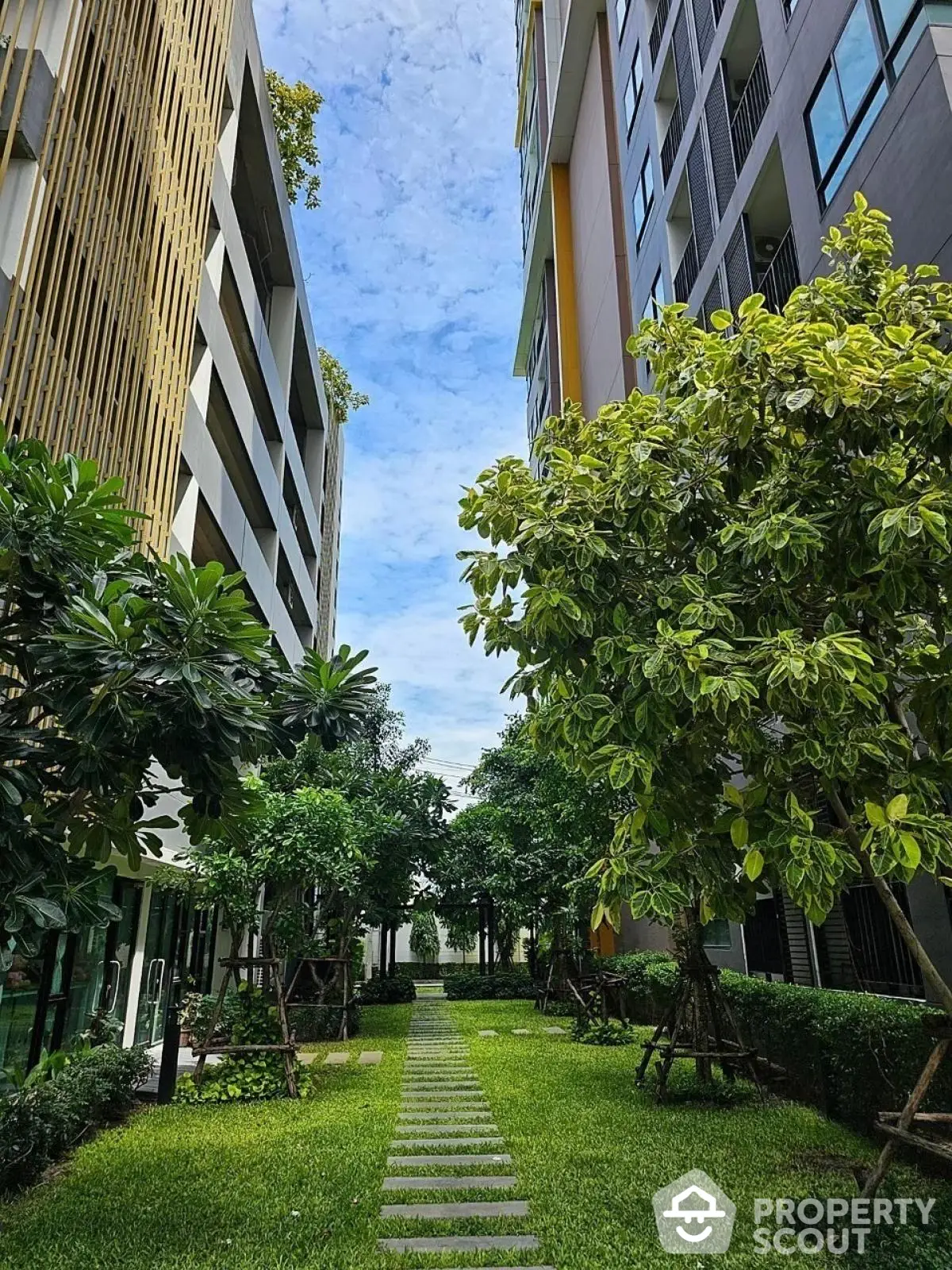 Lush garden pathway between modern high-rise buildings with vibrant greenery.