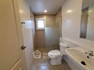 Modern bathroom with sleek fixtures and neutral tiles, featuring a glass shower partition.