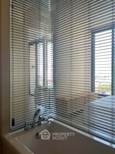 Modern bathroom with sleek blinds and bathtub, offering a glimpse of a bright bedroom view.