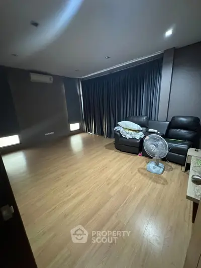 Spacious living room with modern decor and wooden flooring, featuring a comfortable leather sofa and a fan.