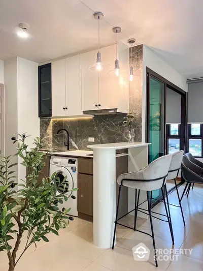 Modern kitchen with washing machine and stylish bar seating in open layout apartment.