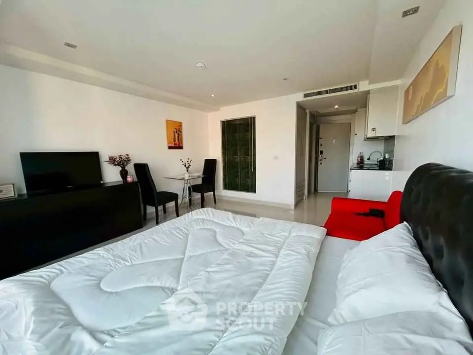 Modern studio apartment with cozy bed, TV, and compact kitchen area.