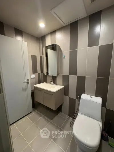Modern bathroom with sleek design and stylish tiles, featuring a wall-mounted sink and contemporary toilet.