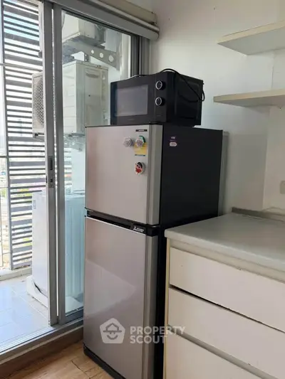 Modern kitchen with fridge and microwave near balcony, featuring sleek design and ample storage space.