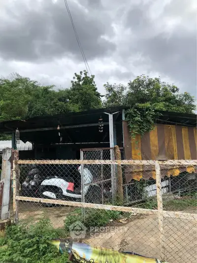 Rustic exterior with overgrown greenery and motorbike under cloudy sky