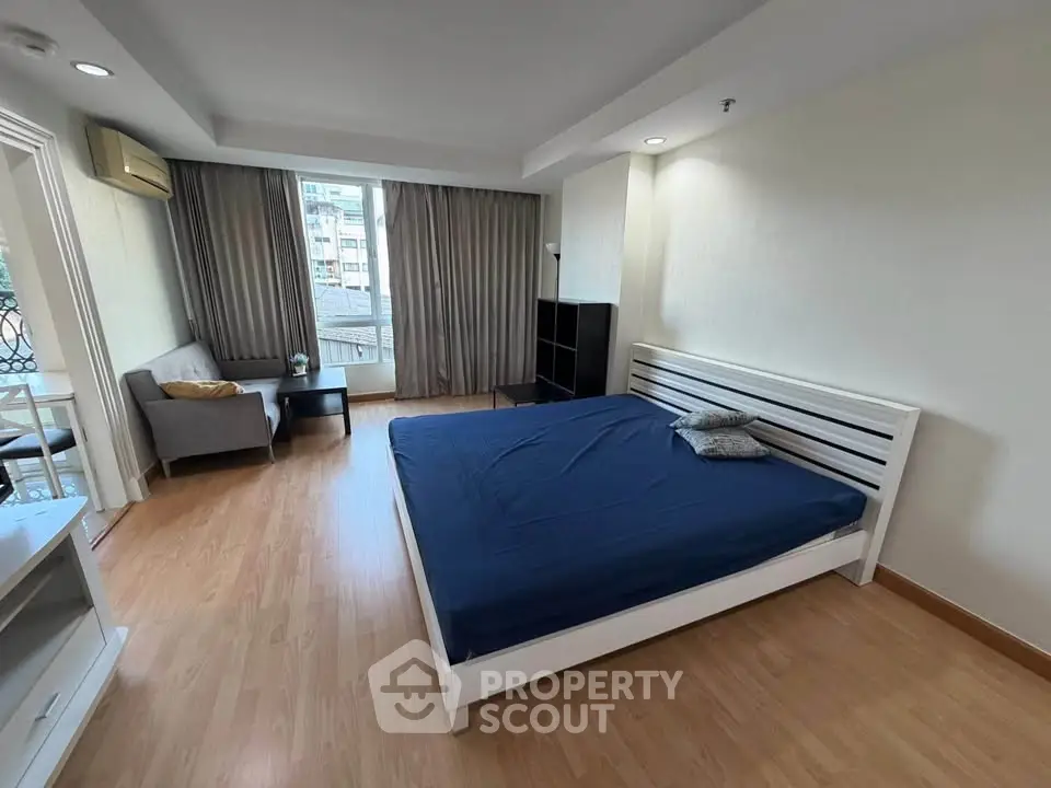 Spacious bedroom with modern furnishings and large window offering city views.