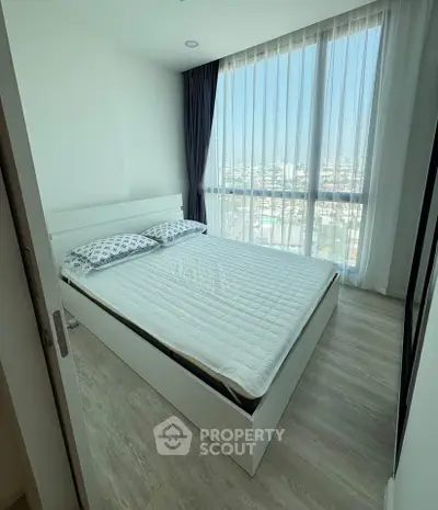 Bright bedroom with large window and city view, featuring modern white bed and wooden flooring.
