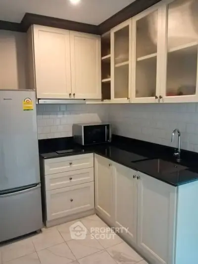 Modern kitchen with sleek black countertops and white cabinetry, featuring a fridge and microwave.