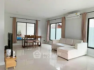 Spacious modern living room with white sofa and dining area, featuring large windows and air conditioning.
