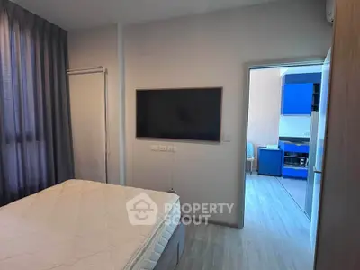 Modern bedroom with wall-mounted TV and view into a stylish kitchen