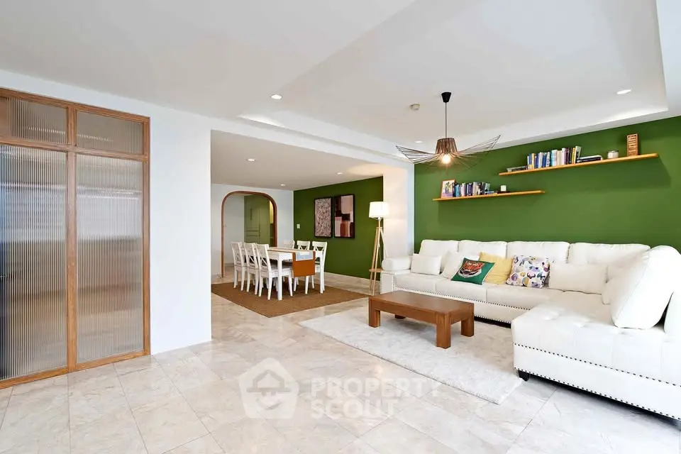 Spacious living room with modern decor and dining area, featuring a cozy white sofa and stylish green accent wall.