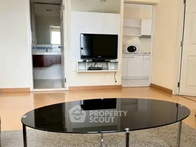 Modern living room with sleek glass coffee table and wall-mounted TV, adjacent to kitchen and bathroom.