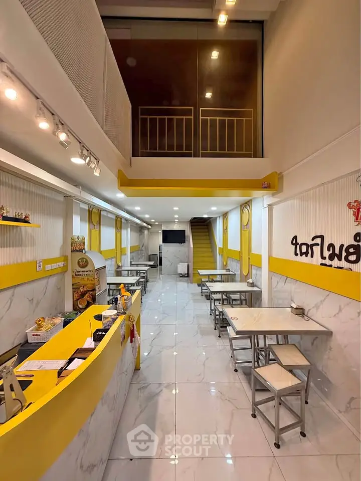 Modern commercial space with high ceilings and bright yellow accents, ideal for a trendy cafe or restaurant.