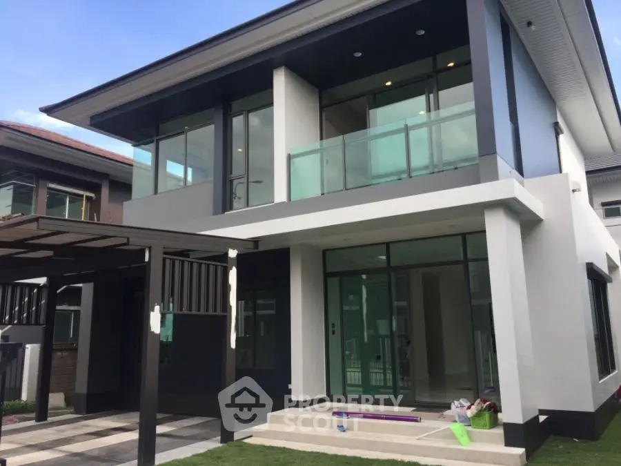 Modern two-story house with large windows and balcony, showcasing sleek architectural design.