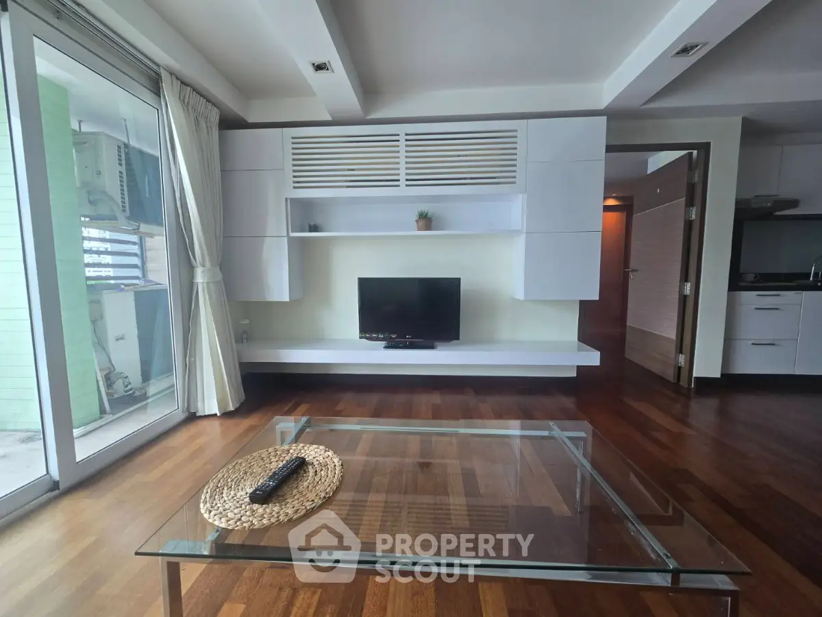 Modern living room with wooden flooring, glass coffee table, and built-in TV unit, offering a stylish and cozy ambiance.