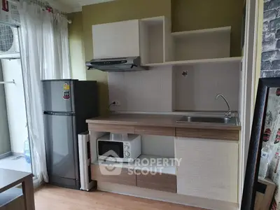 Modern compact kitchen with fridge, microwave, and sleek cabinetry in cozy apartment.