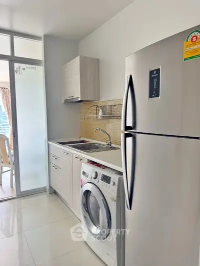 Modern kitchen with stainless steel fridge and washing machine in sleek apartment.