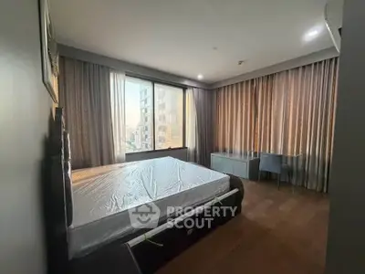 Spacious bedroom with large window offering city views, featuring modern furnishings and ample natural light.