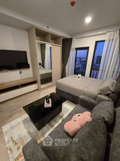 Modern studio apartment with cozy living area and city view, featuring stylish furniture and large windows.