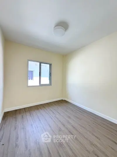 Spacious empty bedroom with wooden flooring and natural light from window.