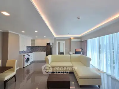 Spacious modern living room with open kitchen, featuring elegant lighting and large windows.