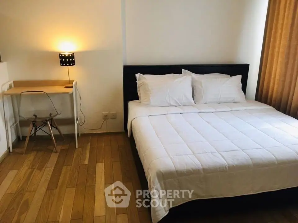 Cozy bedroom with modern decor and wooden flooring, featuring a comfortable bed and a stylish desk lamp.
