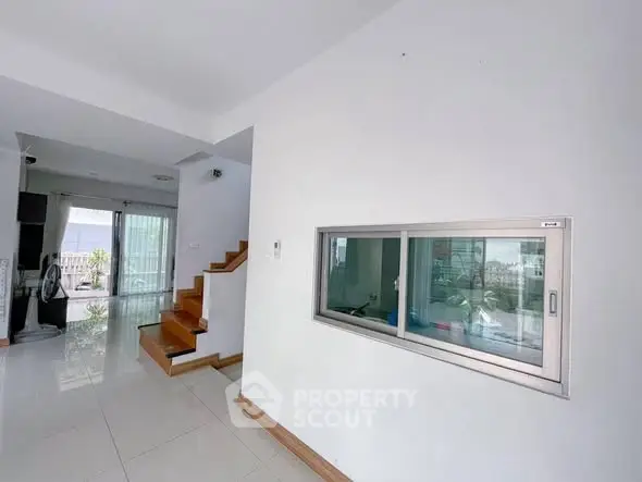 Modern interior with sleek staircase and large window, bright and airy living space.