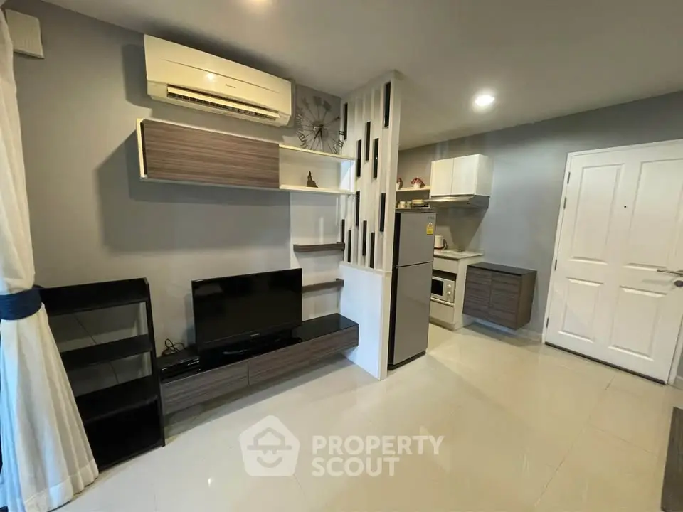 Modern living room with sleek furniture and integrated kitchen area, featuring air conditioning and stylish shelving.