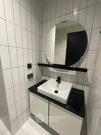 Modern bathroom with sleek sink and round mirror, featuring stylish black and white tile design.