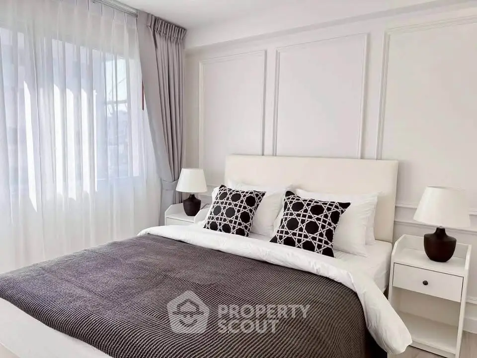 Elegant bedroom with modern decor, featuring a cozy bed, stylish lamps, and natural light through sheer curtains.