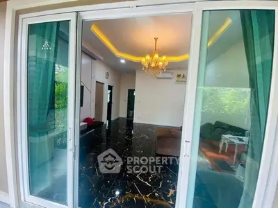 Luxurious living room with marble flooring and elegant chandelier, featuring large sliding glass doors and lush greenery view.