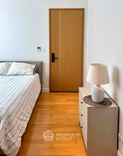 Cozy bedroom with wooden flooring and modern decor, featuring a stylish lamp and comfortable bed.
