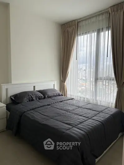 Modern bedroom with large window and city view, featuring elegant curtains and sleek bedding.