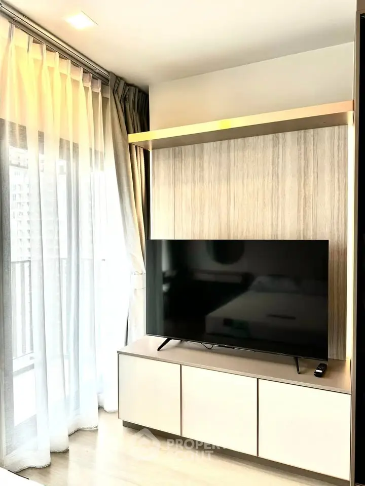 Modern living room with large TV and floor-to-ceiling windows offering natural light.