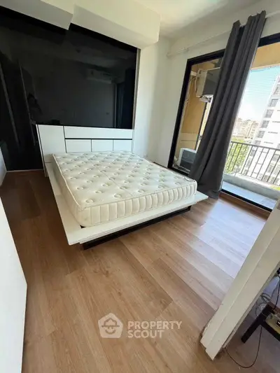 Modern bedroom with large window and balcony access, featuring a stylish bed and sleek flooring.