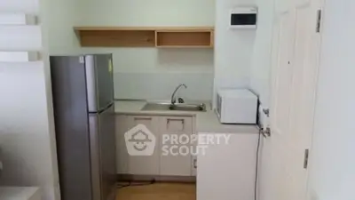 Compact kitchen with fridge, microwave, and sink in modern apartment.