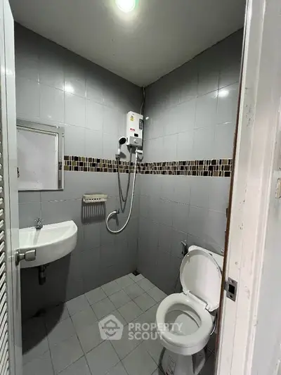 Compact bathroom with shower, toilet, and sink in modern tiled design.