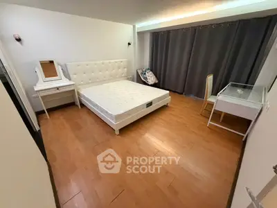 Spacious bedroom with wooden flooring and modern furniture in a cozy apartment.